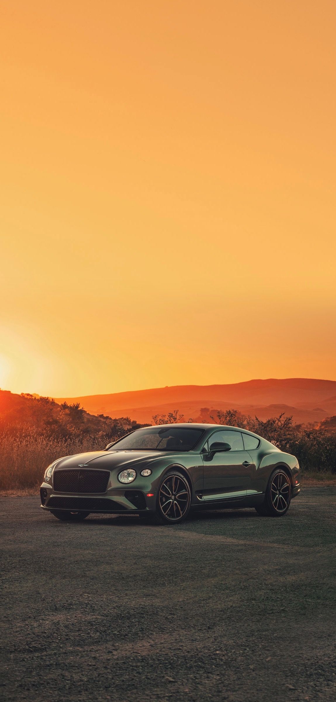 a black car parked in the middle of a field at sunset with mountains in the background