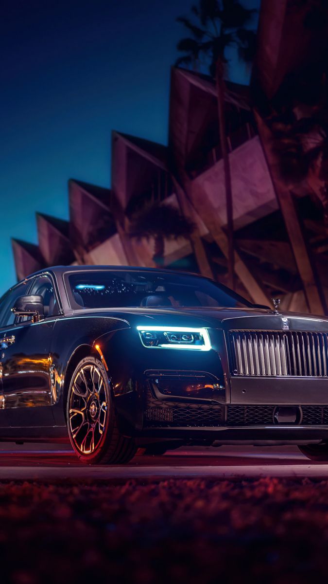 a black rolls royce parked in front of a building at night with red lights on it