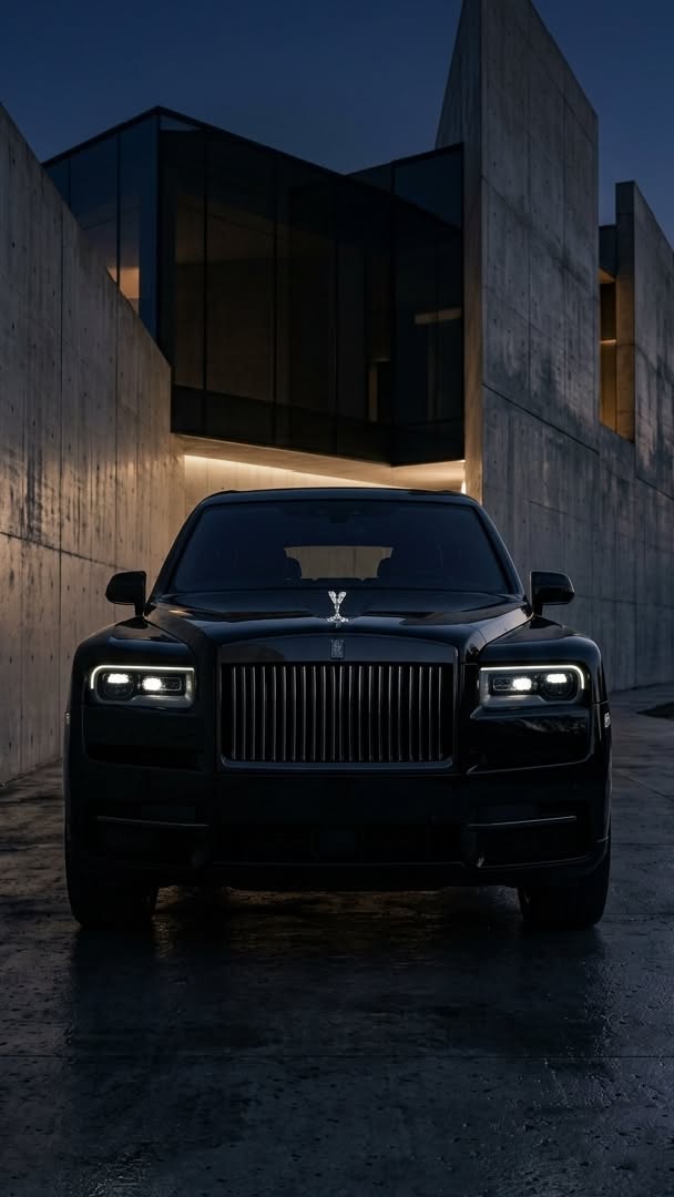 a black rolls royce parked in front of a building at night with the lights on