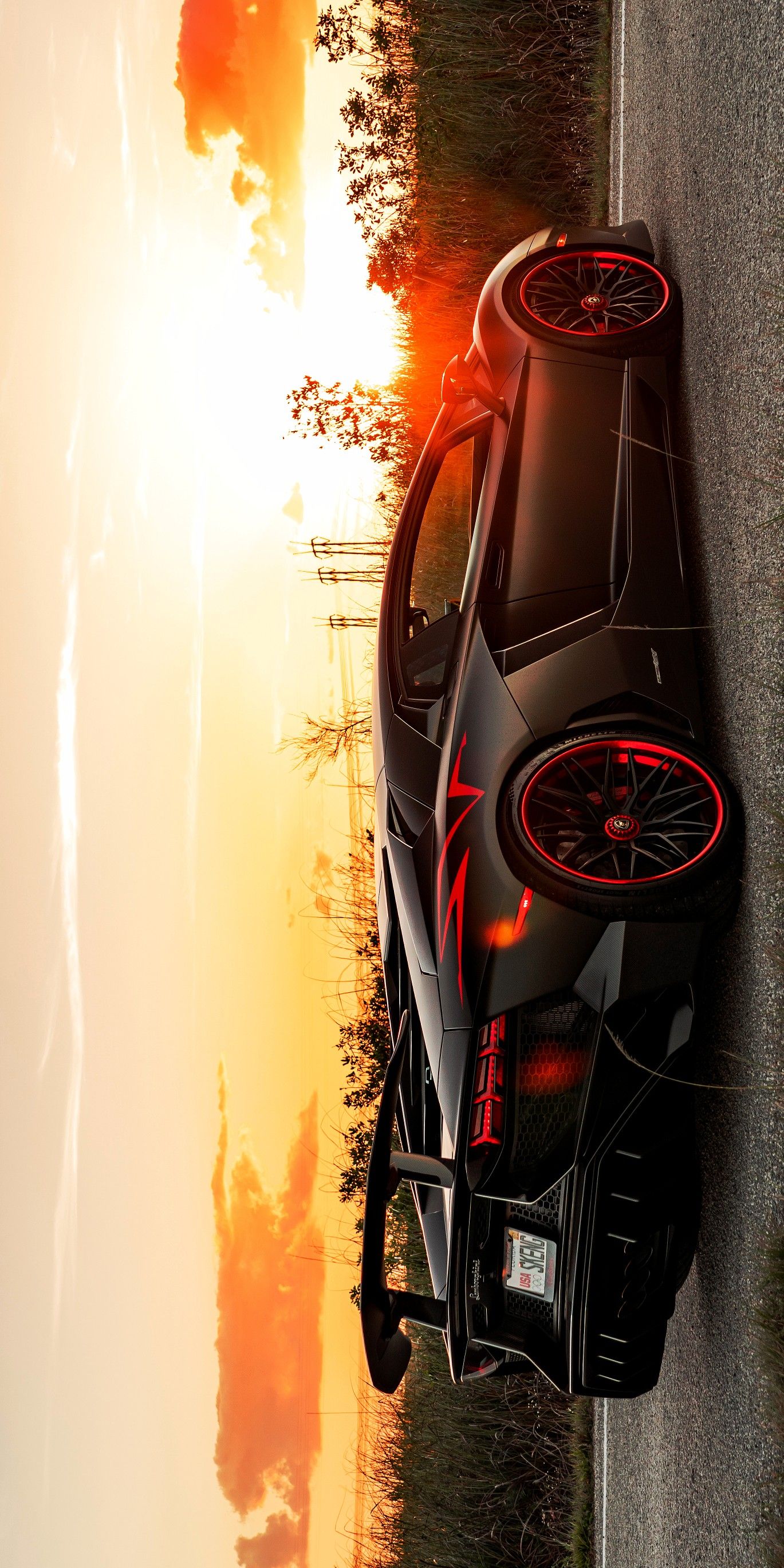 a black sports car driving down a road next to the ocean at sunset or sunrise