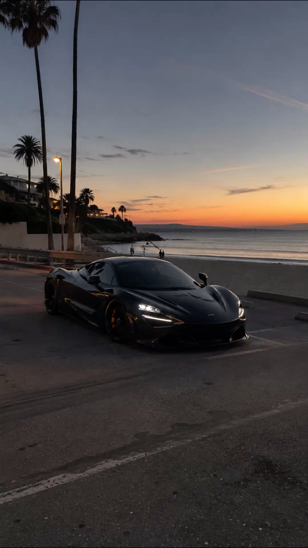 a black sports car is parked on the side of the road near the ocean at sunset