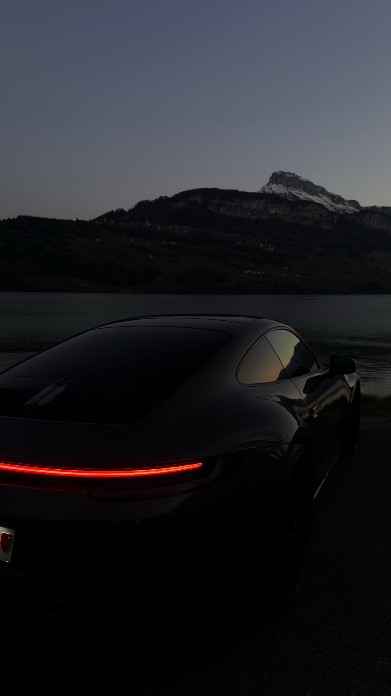 a black sports car parked in front of a body of water at night with mountains in the background