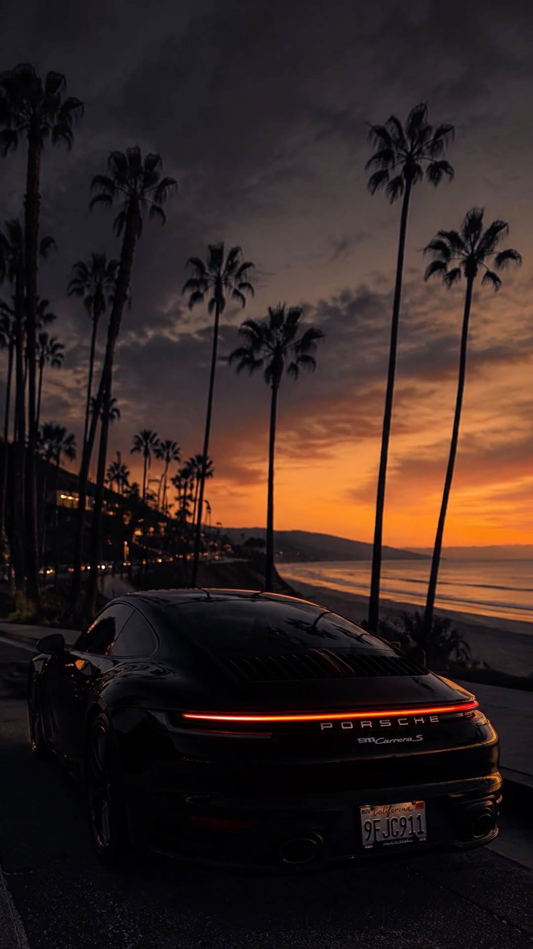 a black sports car parked on the side of the road at night with palm trees