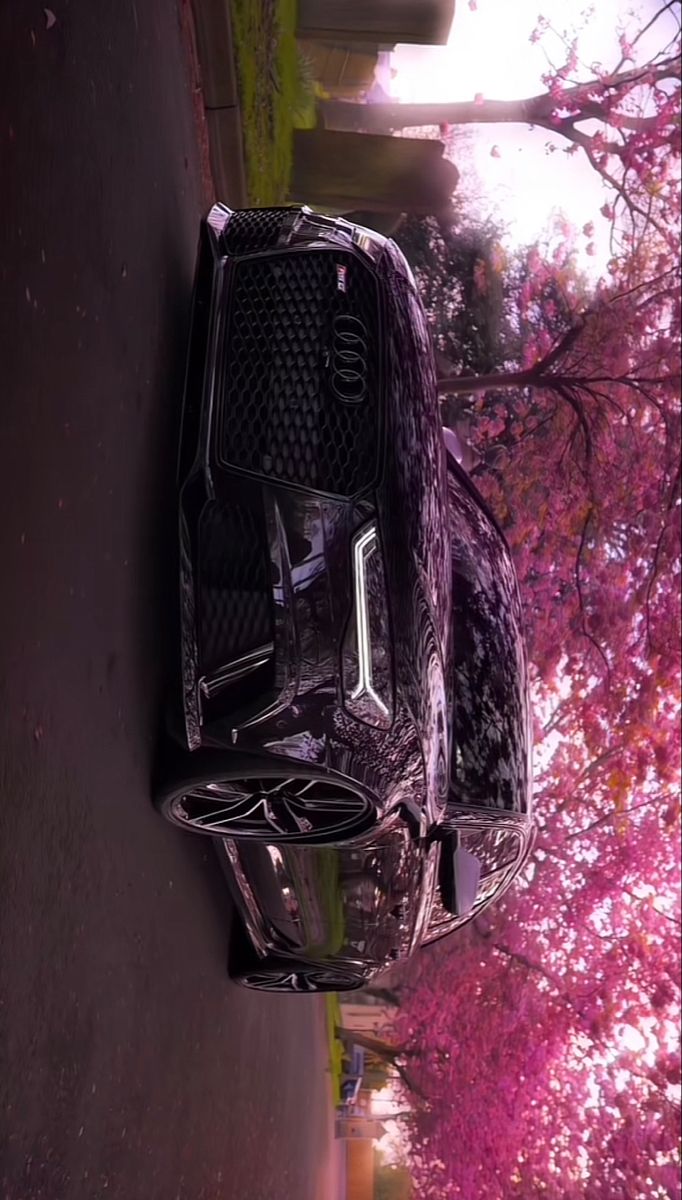 a car parked on the side of a road next to a tree with pink flowers