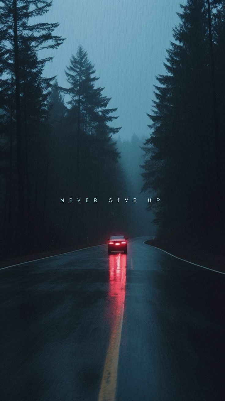 a red car driving down a wet road in the rain with trees on both sides