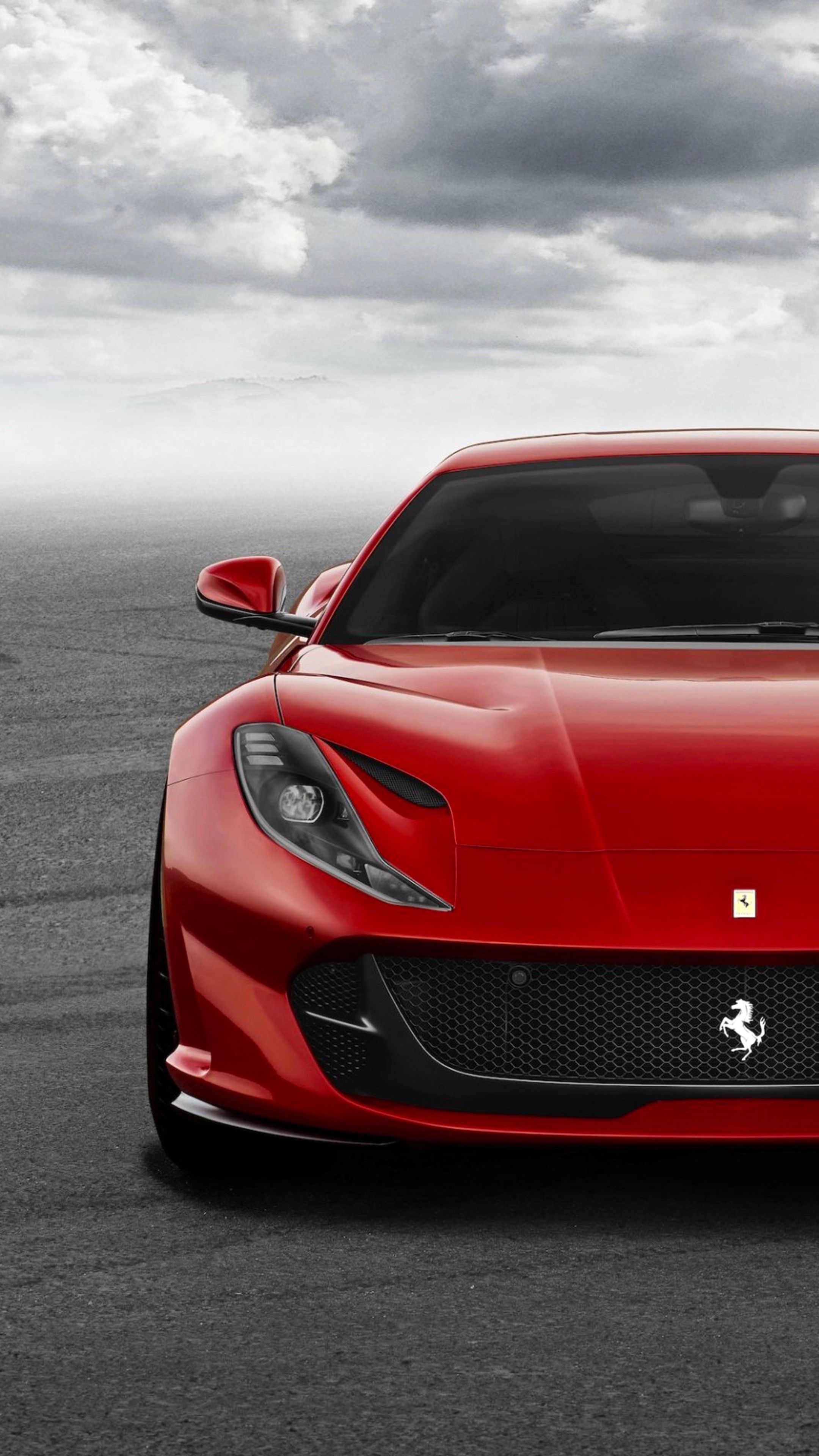 a red ferrari sports car parked on top of a parking lot with dark clouds in the background
