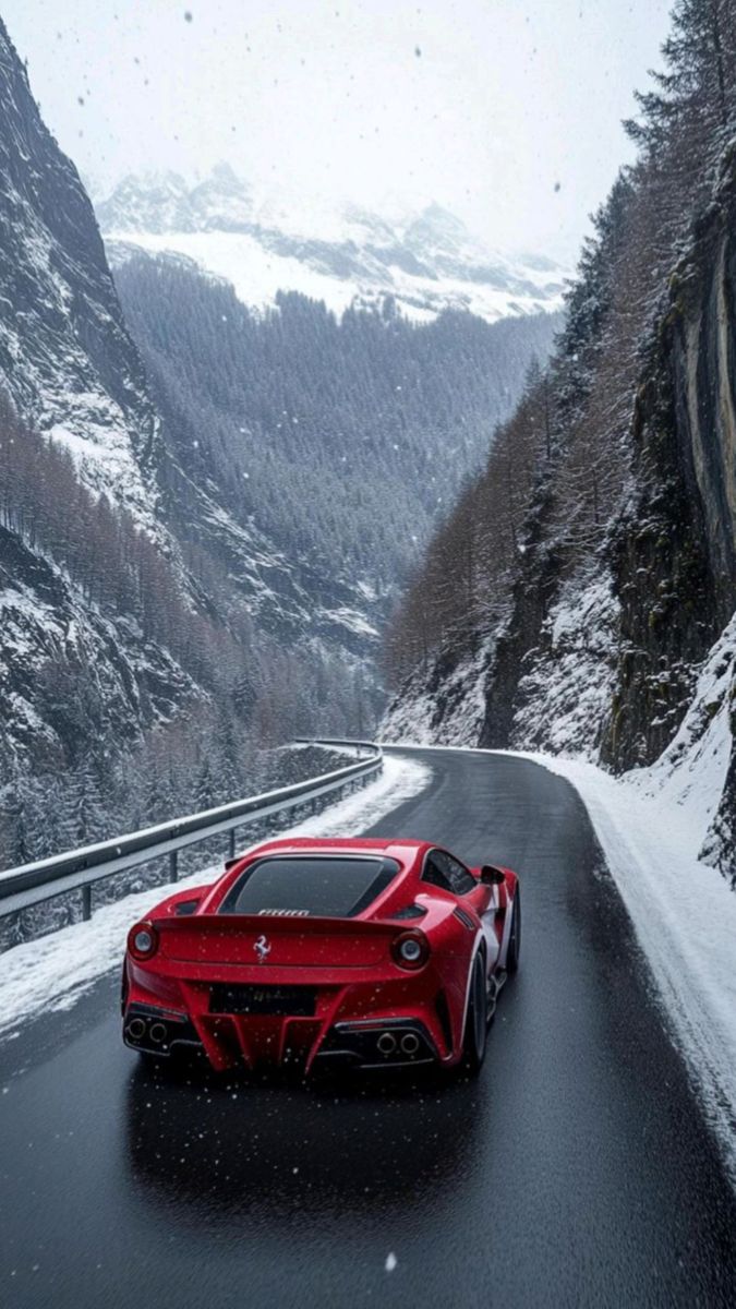 a red sports car driving down a snowy road in the middle of mountains and trees