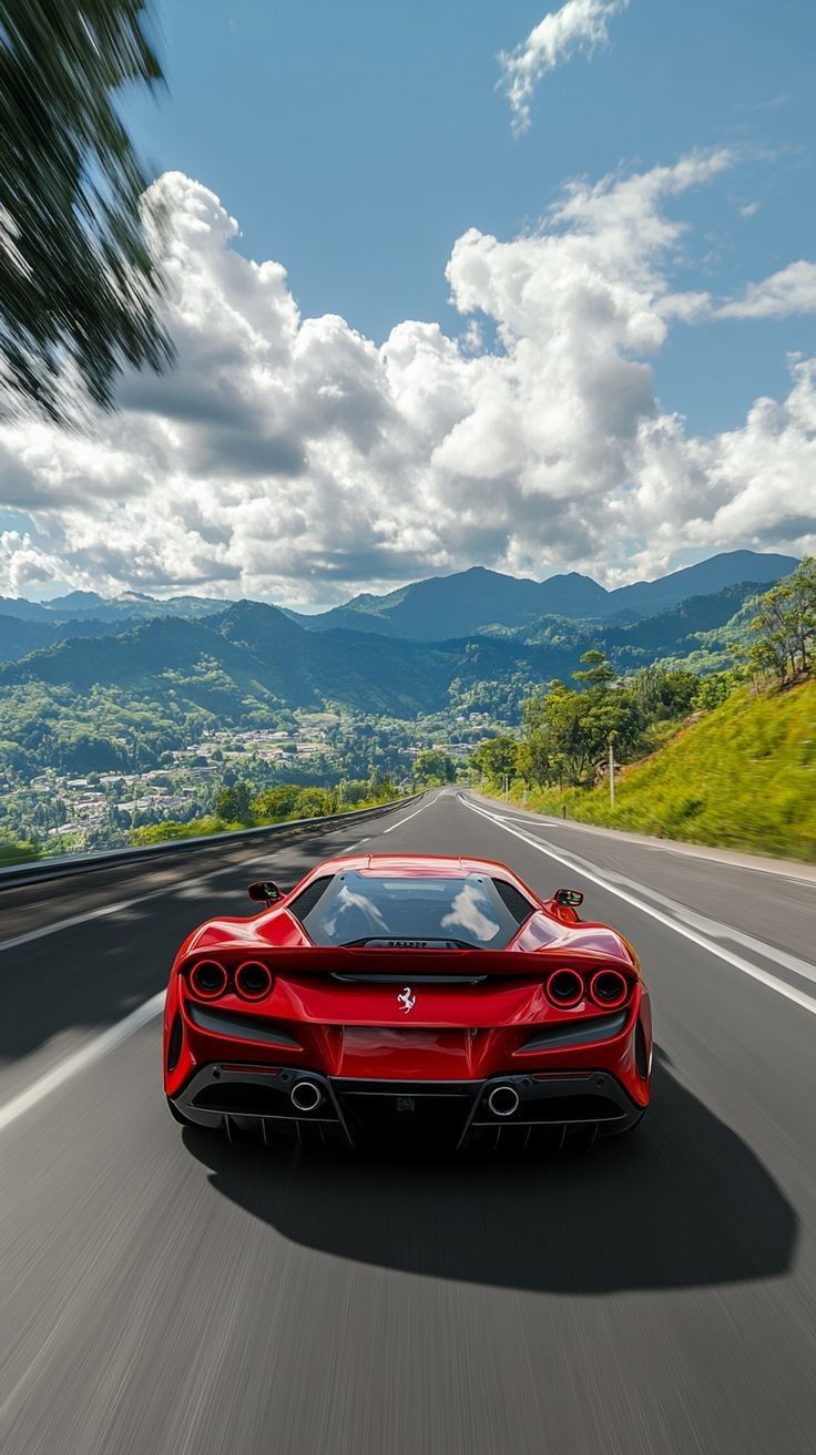 a red sports car is driving down the road with mountains in the backgroud