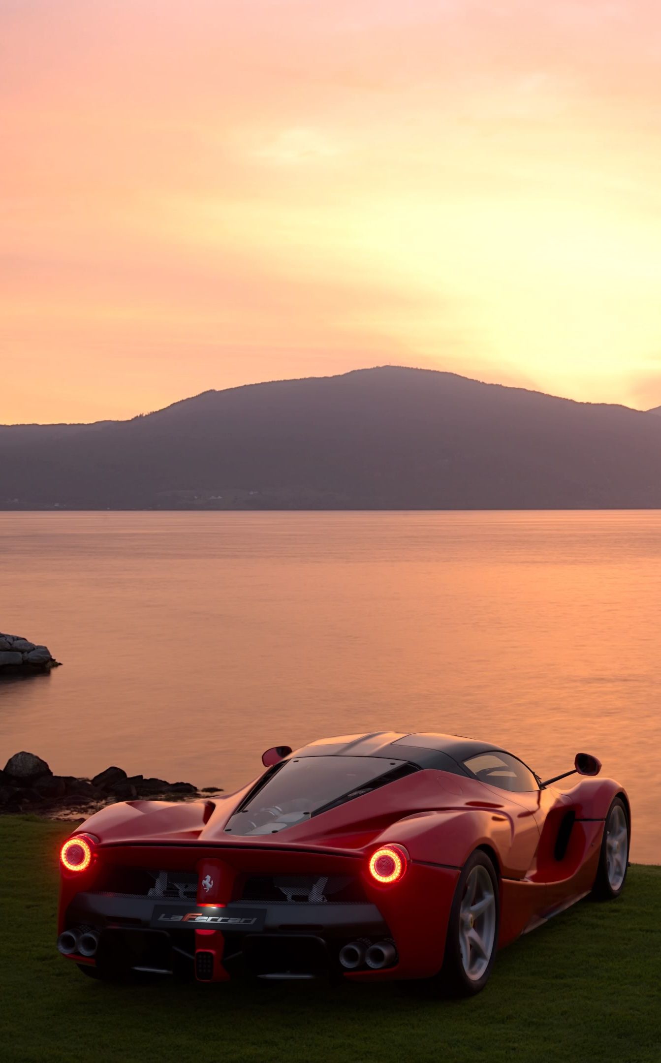 a red sports car parked on top of a lush green field next to the ocean
