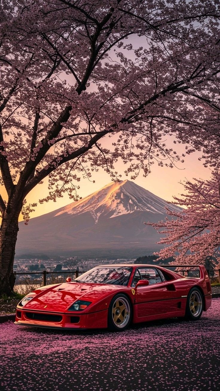a red sports car parked under a cherry blossom tree in front of a snow capped mountain