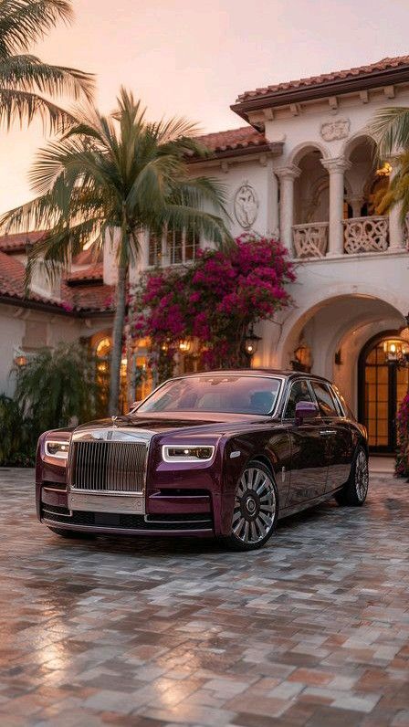 a rolls royce parked in front of a house with palm trees and flowers around it