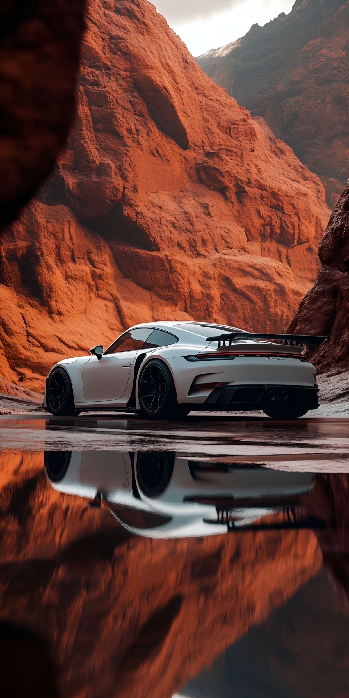 a white sports car is parked in front of some mountains and water with its reflection on the surface