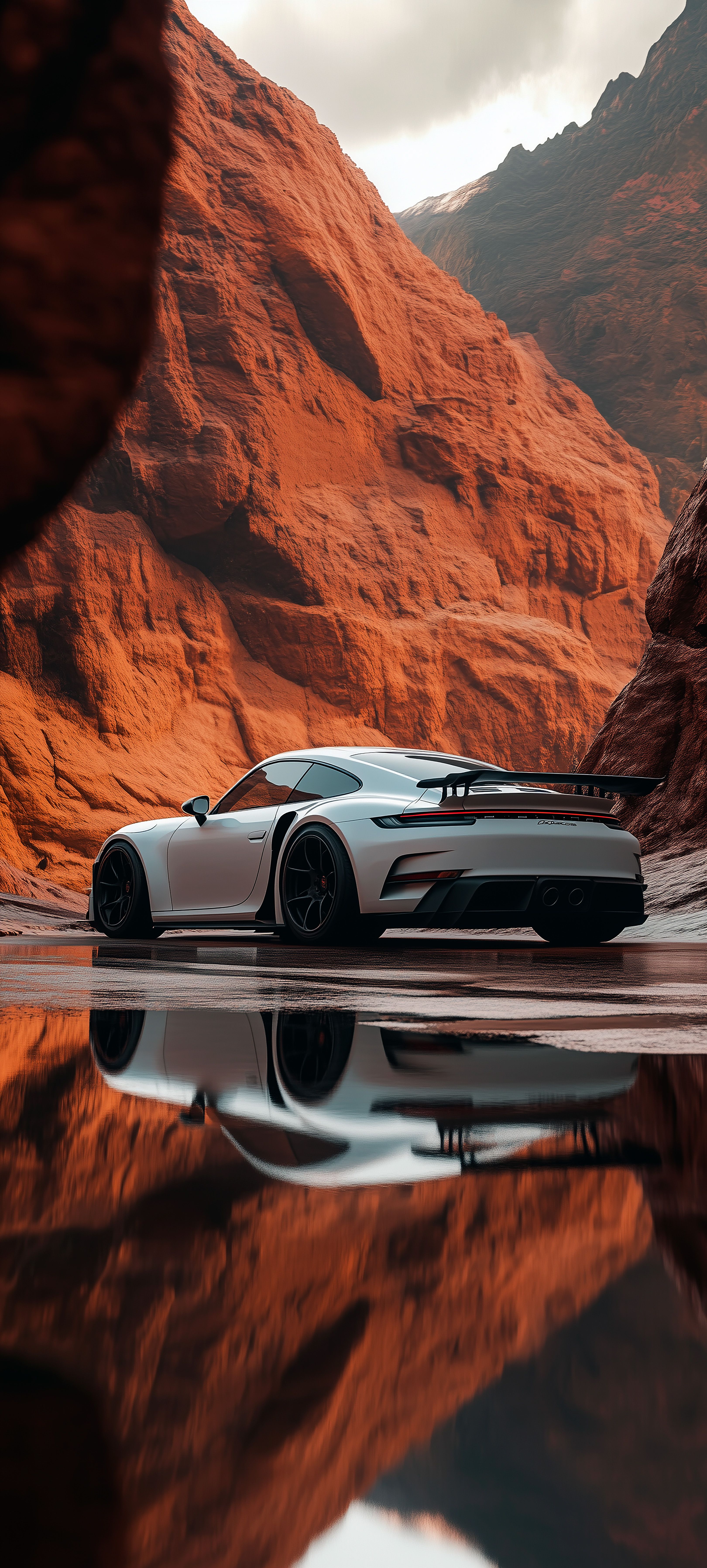 a white sports car is parked in front of some red rocks and water with mountains in the background
