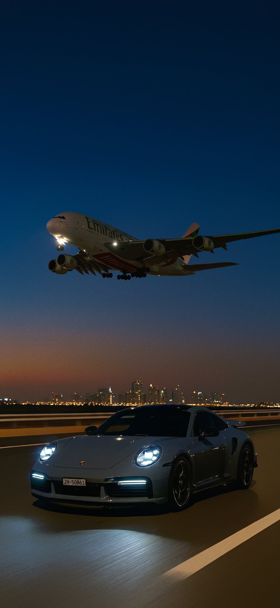 an airplane is flying over a car on the runway at night with it's lights on