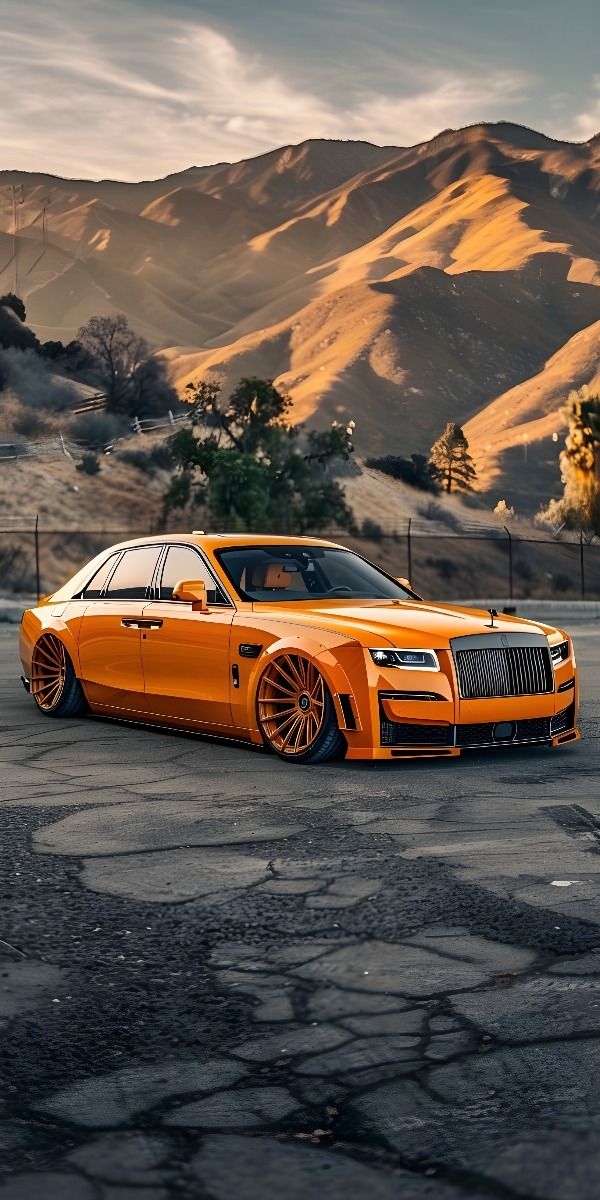 an orange rolls royce parked on the side of a road in front of some mountains
