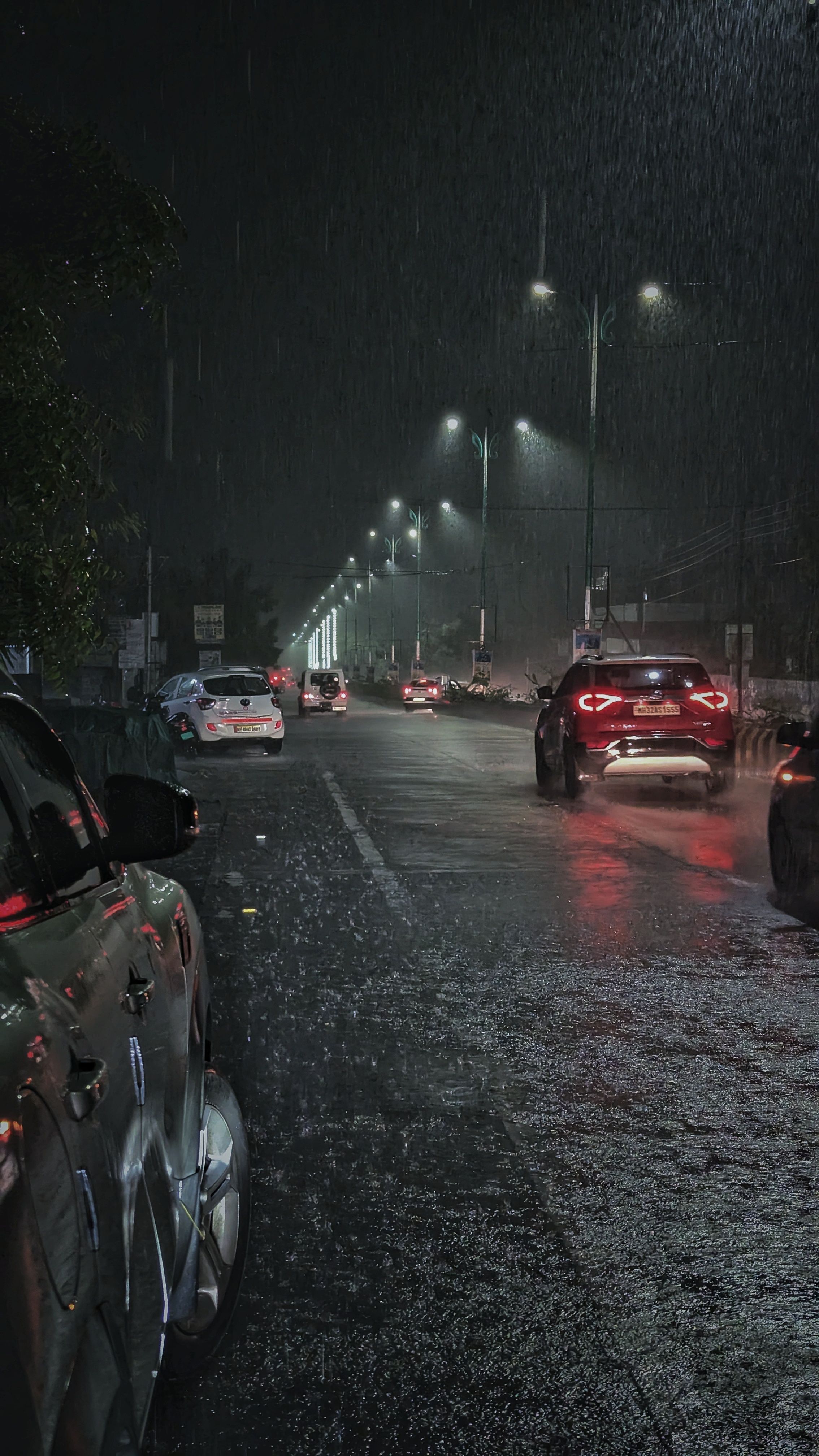 cars are driving down the street in the rain at night time, with lights on