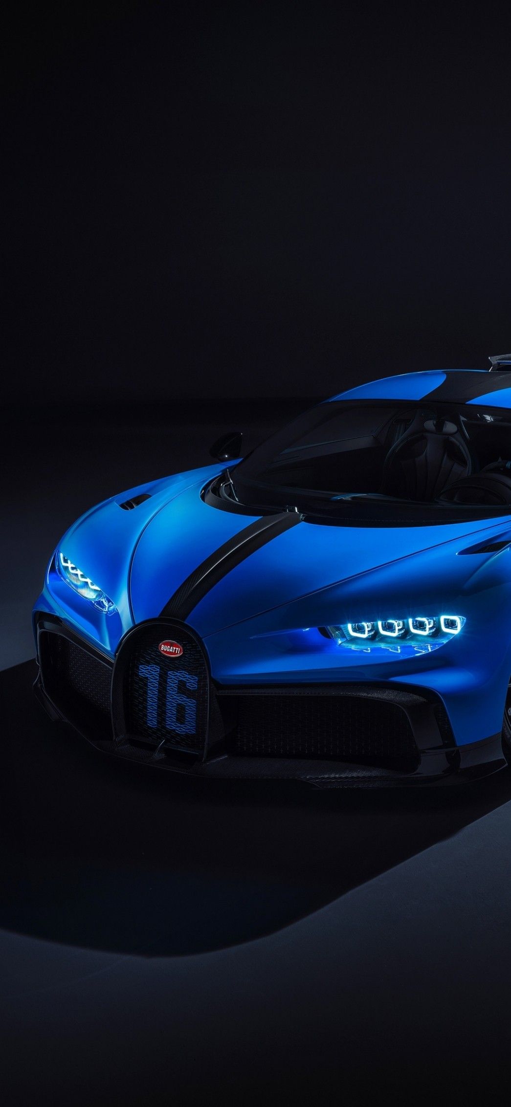 the bugatti supercar is blue and black in this dark room with its hood up