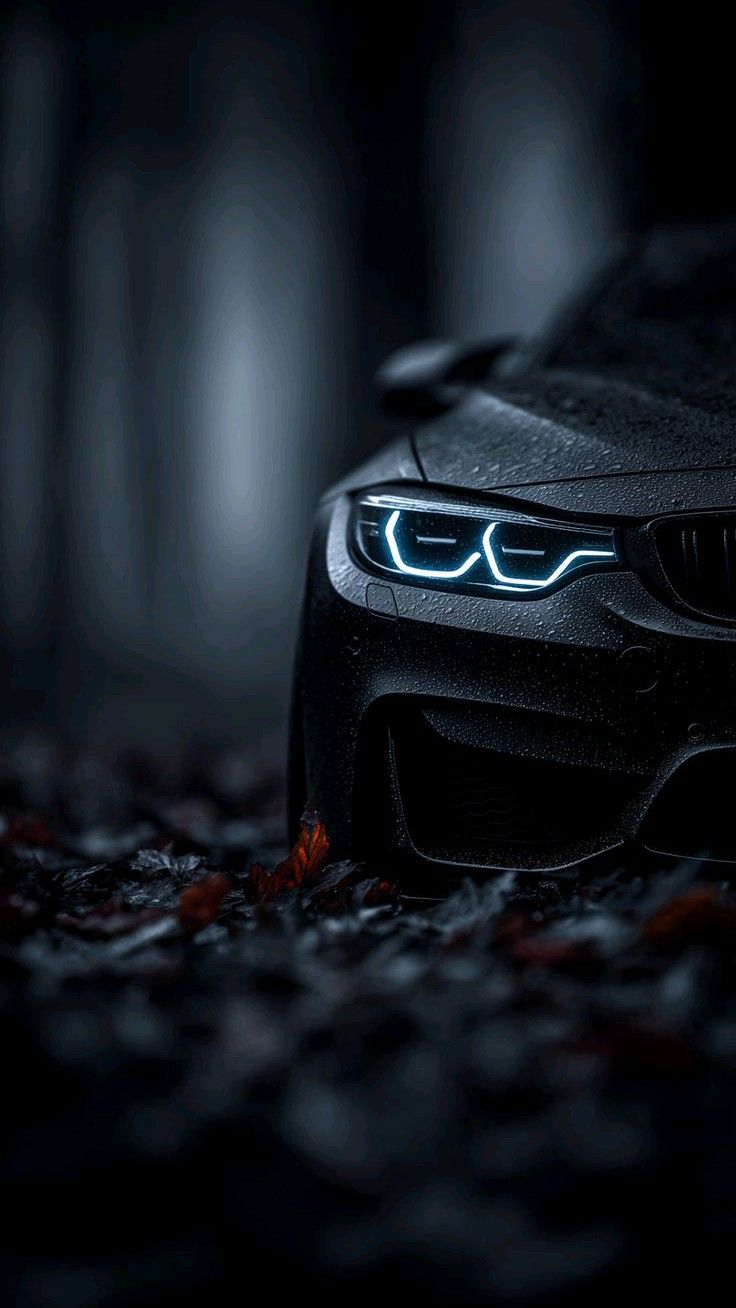 the front end of a black bmw car with its lights turned on in the dark