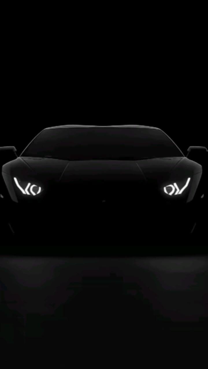 the front end of a black sports car with its headlights turned on at night time