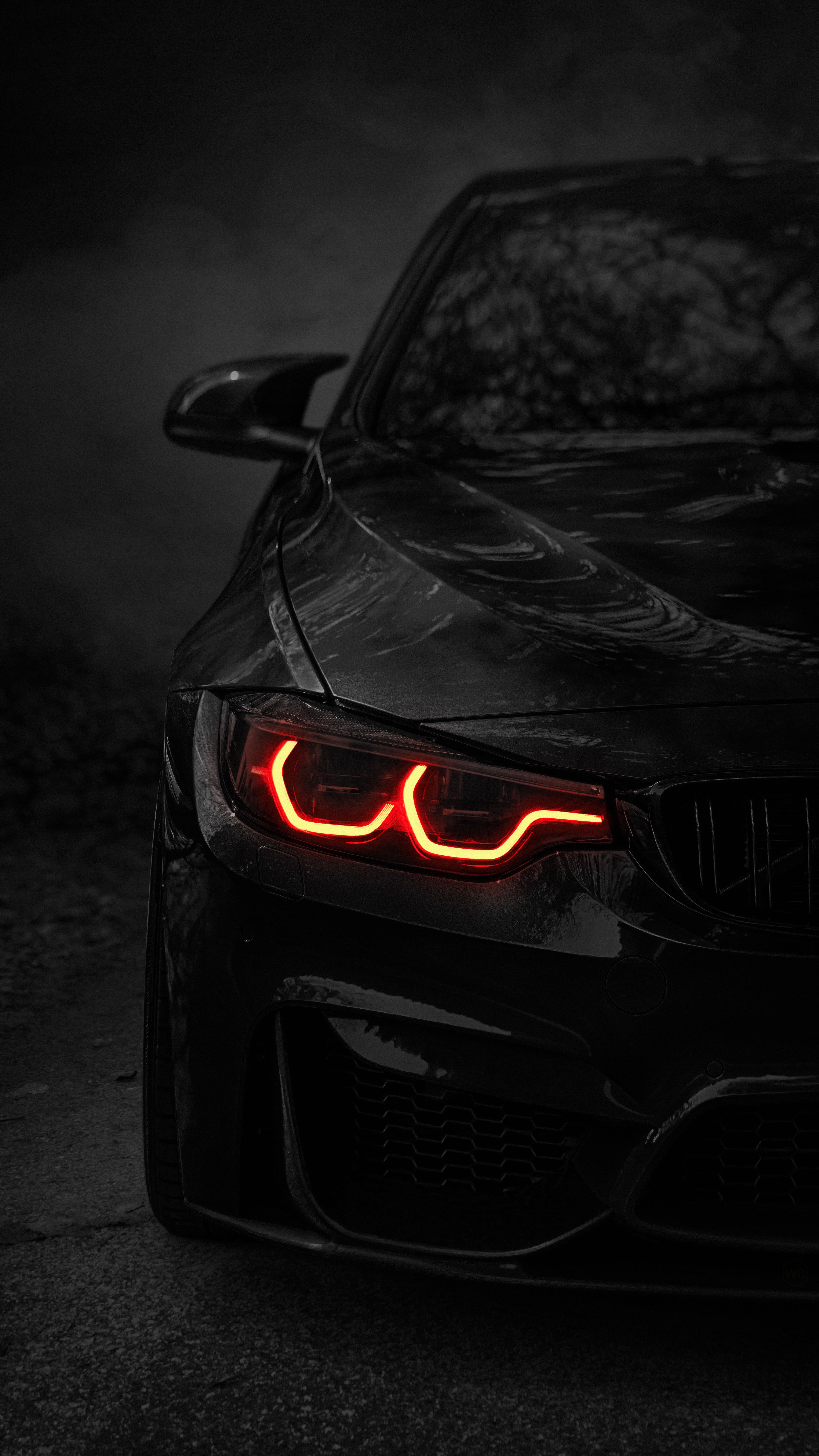 the front end of a black sports car with its lights turned on in the dark