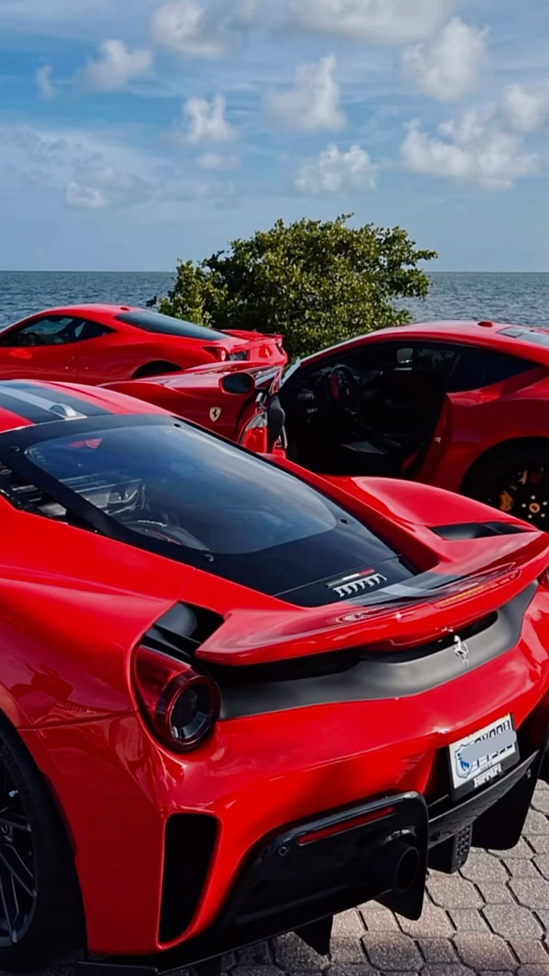 two red sports cars parked next to each other on a brick road near the ocean